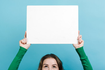 Closeup girl holding a white board copy space above her head against blue background