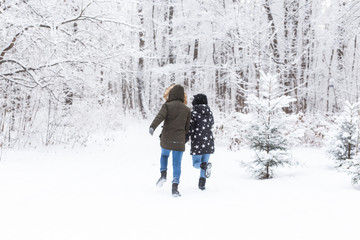 A young and beautiful couple is having fun in the snowy park, running and holding hands. Valentine's Day concept. Winter season.