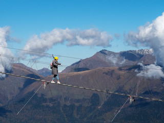 A girl walks on a suspension bridge against a blue sky and a mountain cliff
