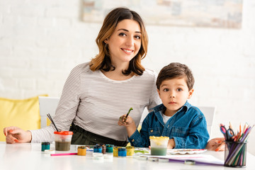 Fototapeta premium happy mother and son looking at camera while drawing with paints together