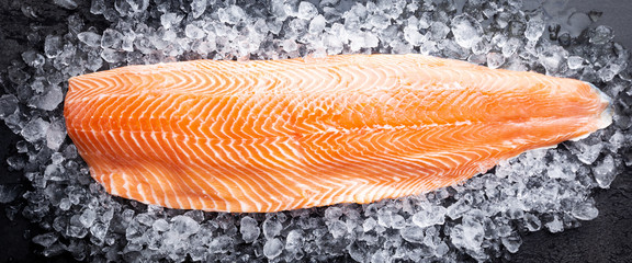 Fresh raw salmon or trout sea fish fillet on ice on black background, top view