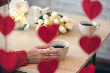 Valentines day concept. Cropped of lonely woman sitting on the table with bouquet of flowers tulips and celebrating in restaurant. View through a heart-shaped garland.