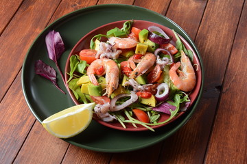Sea food salad with shrimps, avocado, cherry tomatoes, red hot chilly pepper, red onion, arugula, beet leaves,rukola.balsamic sauce in a plate on a wood background Healthy sea food concept
