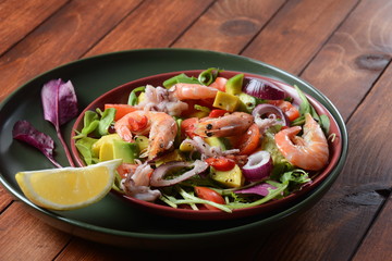 Sea food salad with shrimps, avocado, cherry tomatoes, red hot chilly pepper, red onion, arugula, beet leaves,rukola.balsamic sauce in a plate on a wood background Healthy sea food concept