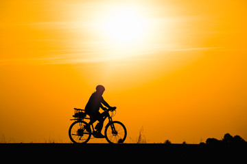 Fototapeta na wymiar Silhouette woman cycling on sunset background