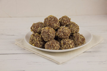 Energy balls homemade healthy candies without sugar in a white plate on a cotton napkin on a white wooden background