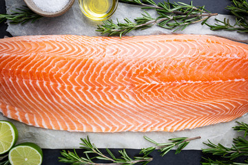 Fresh raw salmon or trout sea fish fillet with spices and herbs on black background, top view