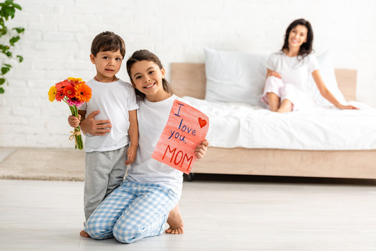 selective focus of children holding i love you mom card near mother sitting in bed