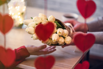 Valentines day.  Close-up of woman and man celebrating in restaurant. Boyfriend giving bouquet of flowers tulips to girlfriend. View through a heart-shaped garland. love, romance, date