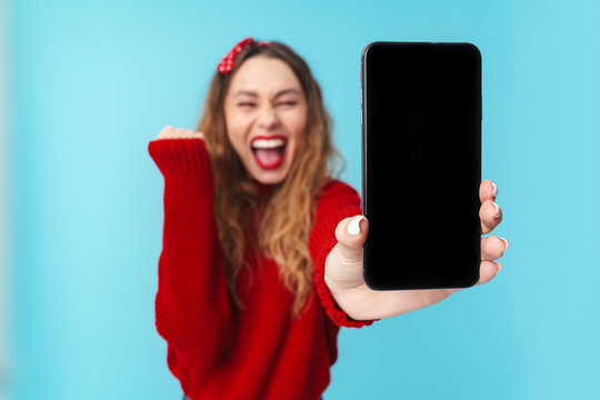Image of delighted woman showing cellphone and making winner gesture