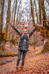 Fototapeta premium Blonde girl throwing red leaves in a beautiful forest