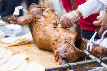 Cutting the mutton hulk fried on a grill for the pilaf. Male hands keep a knife in gloves and cut meat