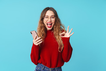 Image of joyful woman holding cellphone and gesturing ok sign