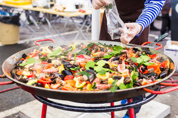 Street food concept - Gourmet seafood paella with pink marine prawns and mussels on yellow saffron rice with peas and bell peppers