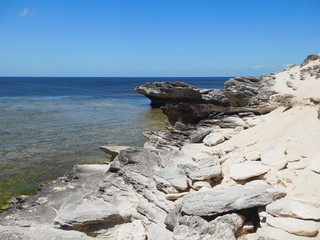 Fototapeta na wymiar Rocky coastline on Rottnest Island, rocky and sandy foreground with clear blue sea and summer clear blue sky