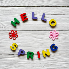 Multi-colored wooden letters making up the words Hello spring and multi-colored wooden flowers on a white wooden background. Top view. Bright spring background. 