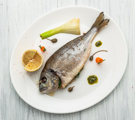 Grilled fish on platter isolated on white. Top view of whole roasted dorado