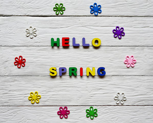 Multi-colored wooden letters making up the words Hello spring and multi-colored wooden flowers on a white wooden background. Top view. Bright spring background. 