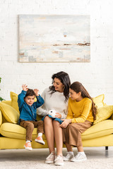 Obraz premium happy children and cheerful mother sitting on sofa with white funny rabbit