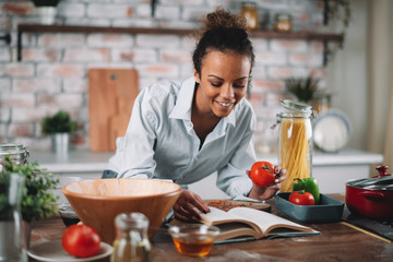 Young woman in kitchen. Beautiful mixed race woman following recipe and cooking.  