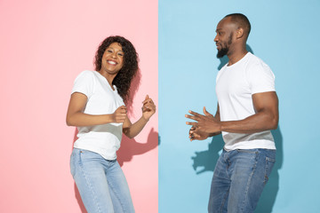 Crazy happy dancing. Young emotional man and woman in casual clothes on pink, blue bicolored background. Concept of human emotions, facial expession, relations, ad. Beautiful african-american couple.