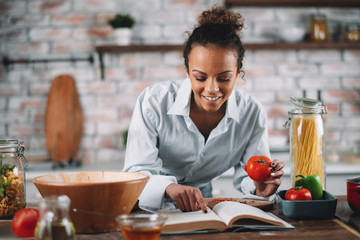 Young woman in kitchen. Beautiful mixed race woman following recipe and cooking.  