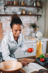Young woman in kitchen. Beautiful mixed race woman following recipe and cooking.  