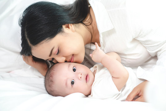 Asian mother kiss her baby son in the bed. Mother faces are smiling happily. The baby looked at the camera.
