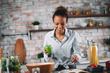 Young woman in kitchen. Beautiful mixed race woman following recipe and cooking.  