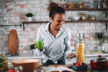 Young woman in kitchen. Beautiful mixed race woman following recipe and cooking.  