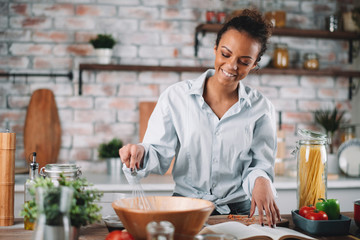 Young woman in kitchen. Beautiful mixed race woman following recipe and cooking.  