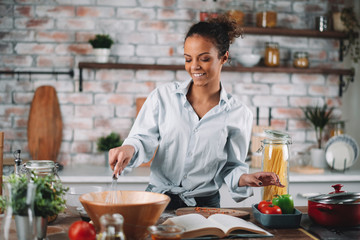 Young woman in kitchen. Beautiful mixed race woman following recipe and cooking.  