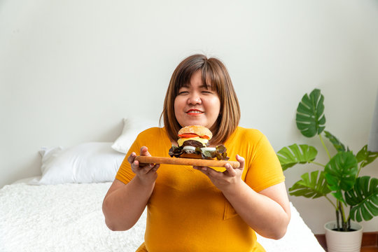 Hungry overweight young asian woman holding hamburger, Her hungry all time and overeat, gluttony and binge eating. Her lifestyle is eating fast food all time. Unhealthy Concept