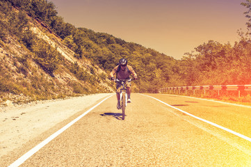 Fototapeta premium Male cyclist riding a bike on mountain road. Toned image