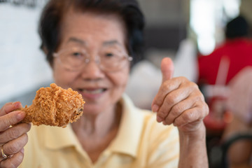 Selective focus of fried chicken, Asian elderly women are eating fried chicken. In the restaurant,...