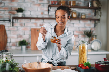 Young woman eating honey. Beautiful mixed race woman in kitchen..