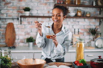 Young woman eating honey. Beautiful mixed race woman in kitchen..