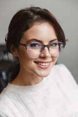 Image of young woman wearing eyeglasses smiling at camera indoors