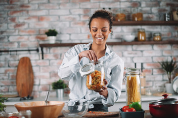 Young mixed race woman in kitchen. Beautiful woman cooking pasta. 