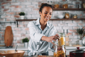 Young mixed race woman in kitchen. Beautiful woman cooking pasta. 
