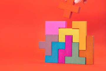 Hand holding piece of wooden block puzzle. wood cube stacking. Concept of complex and smart logical thinking. Slightly defocused and close up shot. on a red background