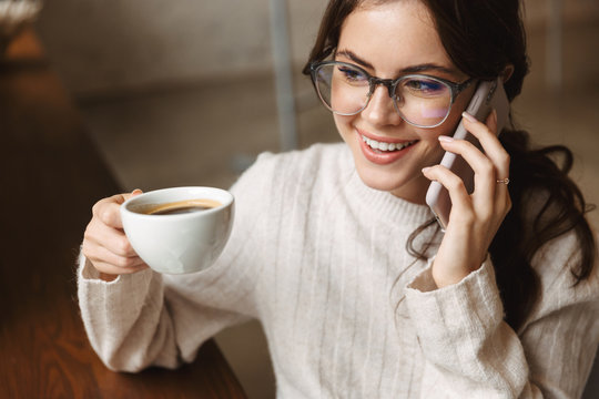 Image of young woman talking on smartphone and drinking cofee in cafe