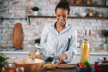 Young mixed race woman in kitchen. Beautiful woman cooking pasta. 