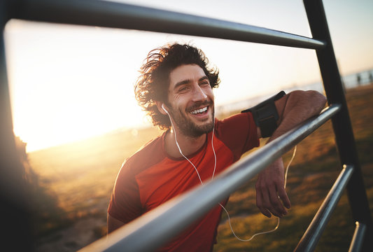Happy fit young male runner enjoying listening to music on earphones during the morning light