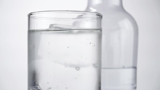Water in a glass with clear ice cubes and a bottle on white Background