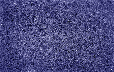 Cleaning sponge rubbing surface close up with blur effect in blue color.