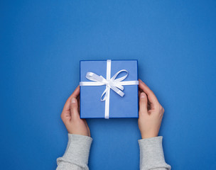 two female hands in a sweater hold a square blue box with a bow