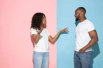 Greeting, smiling. Young emotional man and woman in casual clothes on pink and blue bicolored background. Concept of human emotions, facial expession, relations, ad. Beautiful african-american couple.