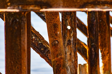 Very rusty metal frames, old thick metal subject to corrosion from salty seawater. Red bright color in sunlight