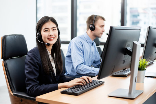 Beautiful Asian female call center employees are working. She turned to look at the camera with a smile. Her friedns working in the background